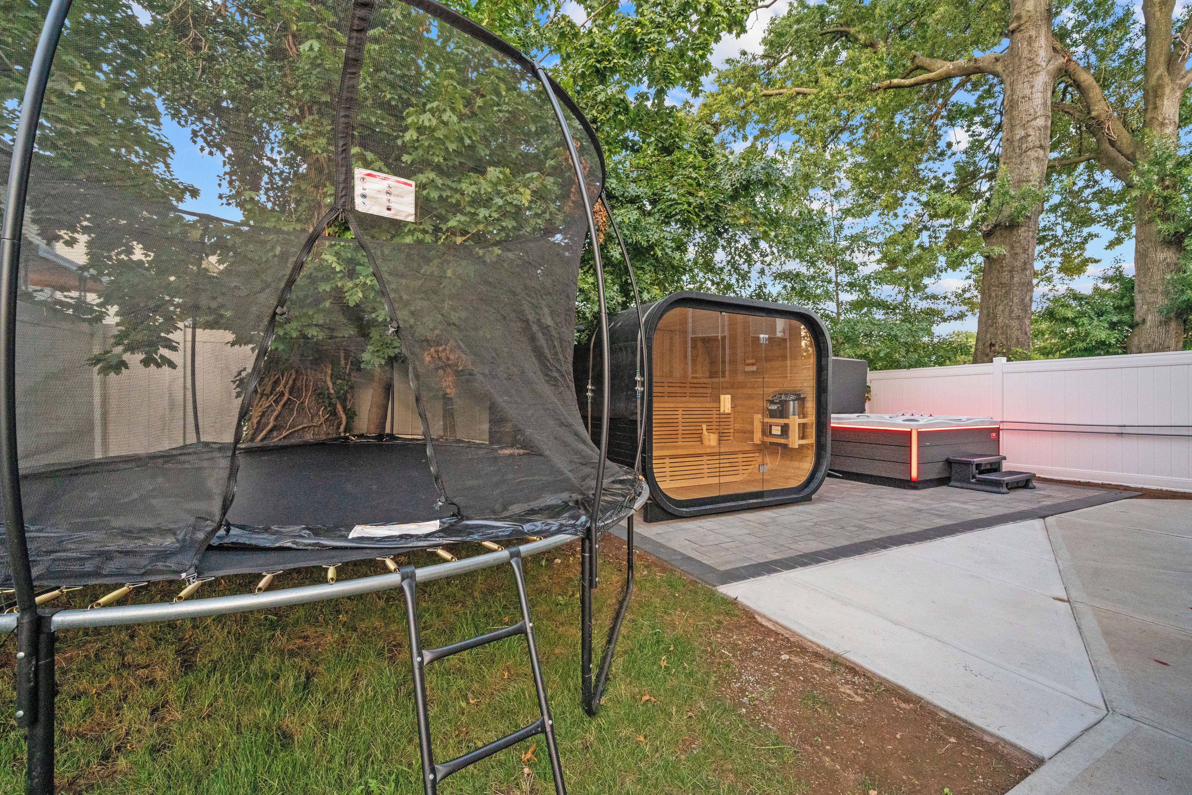 Un trampolín con red de seguridad, un banco de madera y un jacuzzi en un patio trasero.