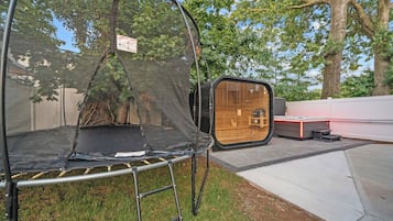 Un trampolín con red de seguridad, un banco de madera y un jacuzzi en un patio trasero.