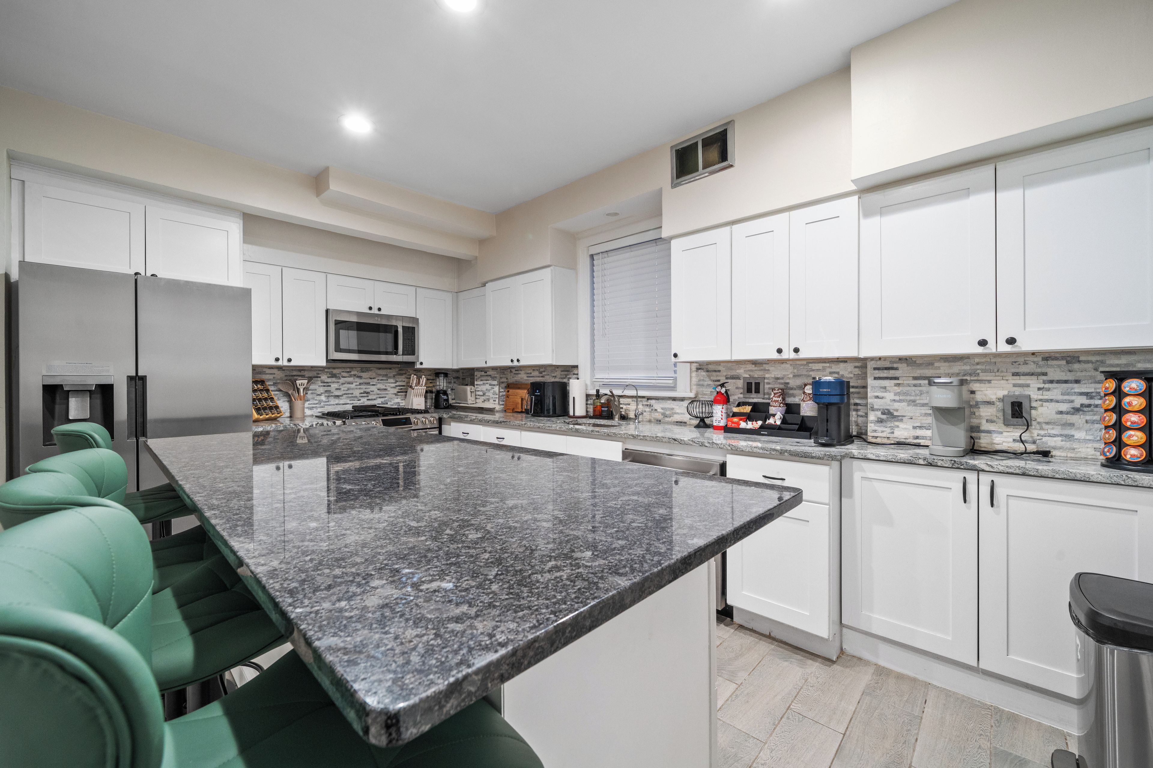 Cocina moderna con gabinetes blancos, encimera de granito y electrodomésticos de acero inoxidable.