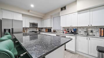 Cocina moderna con gabinetes blancos, encimera de granito y electrodomésticos de acero inoxidable.