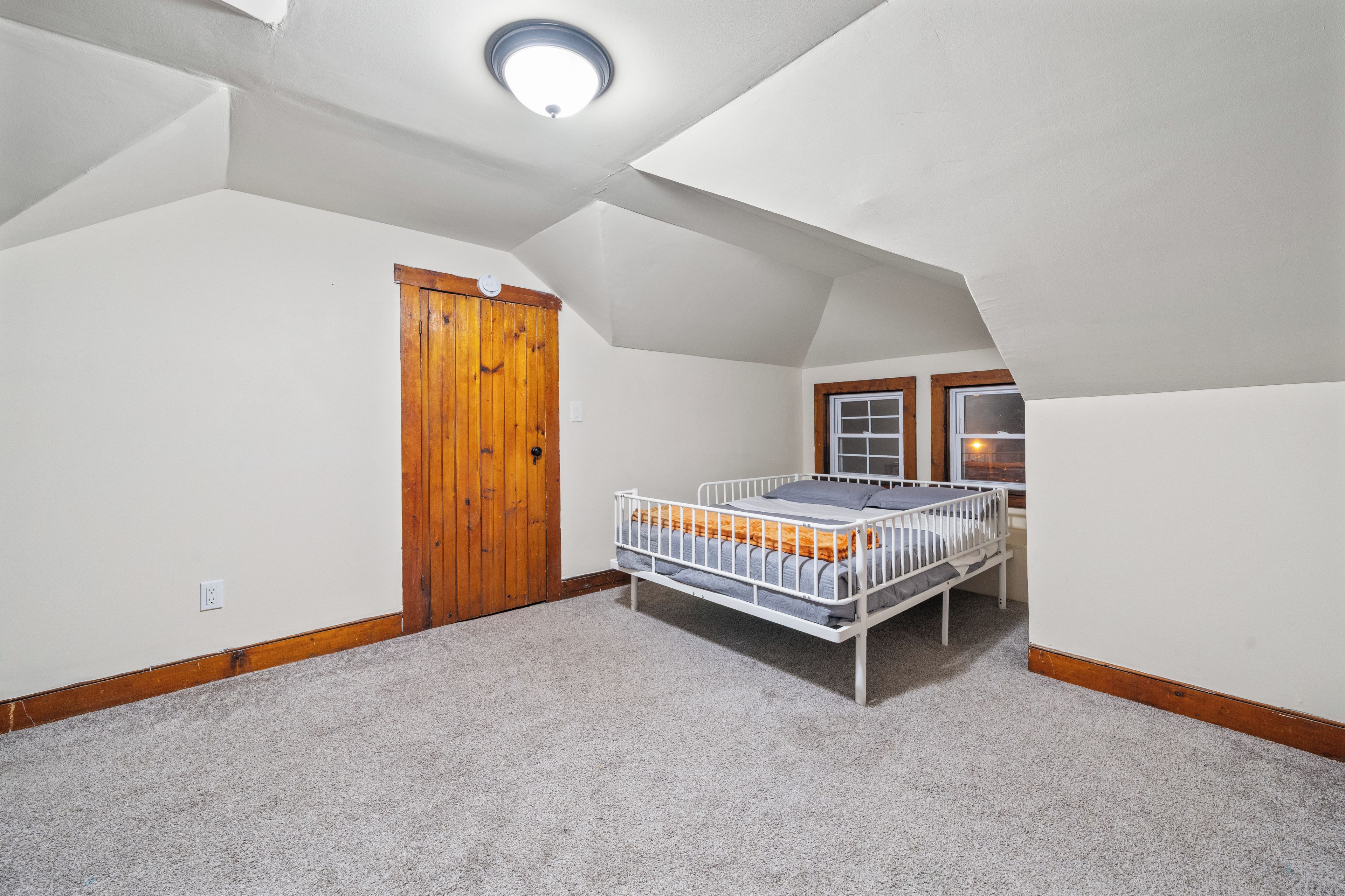 Un dormitorio con techo inclinado, una cama individual, una puerta de madera y una ventana.