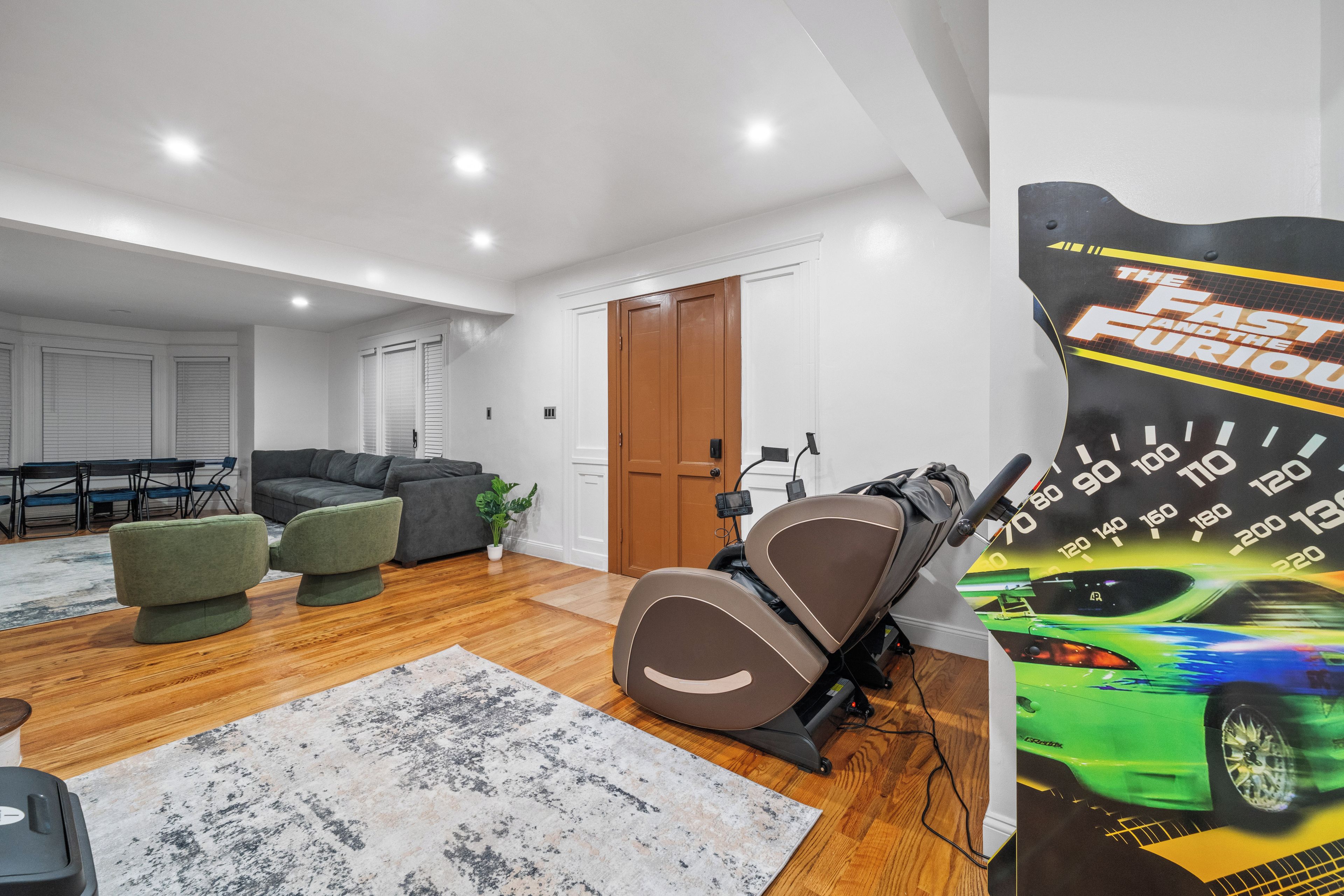 Una habitación con un sofá gris, un sillón verde, una cinta de correr y un cartel de un coche.