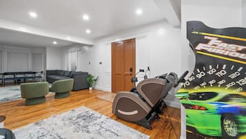 Una habitación con un sofá gris, un sillón verde, una cinta de correr y un cartel de un coche.