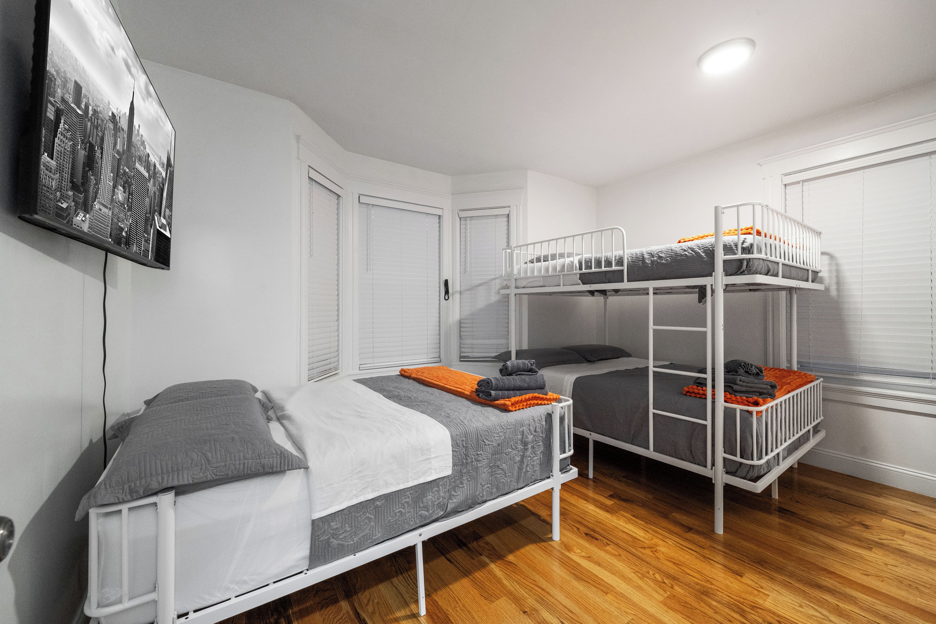 Una habitación con literas, una puerta, una ventana con persianas y un cuadro colgado en la pared.