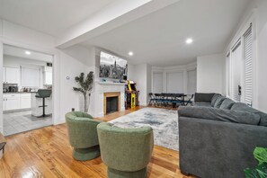 A modern living room with a grey sofa, two green ottomans, a fireplace, and a cityscape painting on the wall.