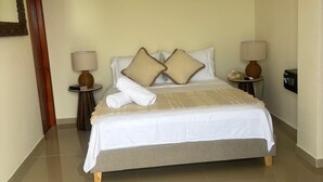 Une chambre d’hôtel avec un lit, deux tables de chevet, une lampe sur chaque table et une porte sur le côté gauche.