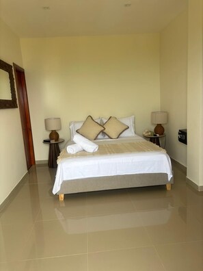 Habitación de hotel con una cama, dos mesitas de noche, una lámpara sobre cada una y una puerta a la izquierda.