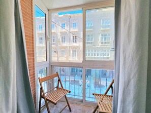 A balcony with two wooden chairs, a glass railing, and a view of a white building with balconies. - Apartamento Alba 4 by Interhome (Cartagena)
