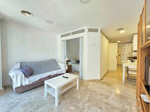 A modern living room with a sofa, a coffee table, and a sliding door leading to a kitchen area. - Apartamento Alba 3 by Interhome (Cartagena)