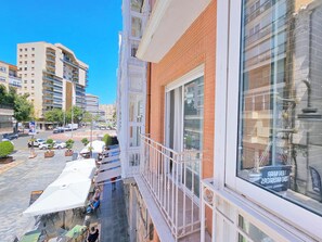 Ein Gebäude mit einem Balkon, der auf eine Straße mit Autos und Bäumen blickt.