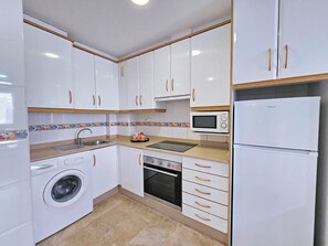 Uma cozinha compacta com armários brancos, máquina de lavar, micro-ondas e geladeira.