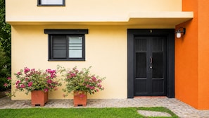 A building with a black door and window, two potted plants with pink flowers, and a number '9' on the door. - Villa Guaduales is where the magic of Colombia meets the peace of home. (Quimbaya)