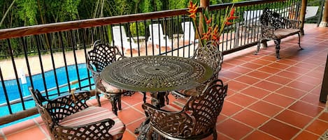 Un patio al aire libre con una mesa redonda y sillas, una piscina al fondo y una barandilla.