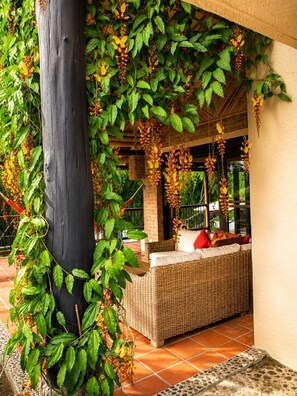 A covered outdoor seating area with wicker furniture and hanging plants. - Villa Guaduales is where the magic of Colombia meets the peace of home. (Quimbaya)
