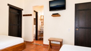 A bedroom with two beds, a TV mounted on the wall, and a wooden bench.