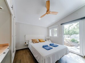 Ein Schlafzimmer mit einem Bett, einem Deckenventilator, einem Fenster und Blick ins Freie.