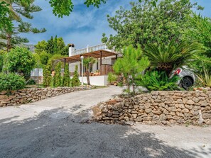 Uma casa com entrada em muro de pedra, um alpendre coberto e um carro estacionado nas proximidades.