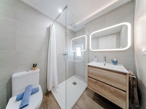 Ein modernes Badezimmer mit einer gläsernen Duschkabine, Toilette, Waschbecken mit Spiegel und einem Holzschrank.