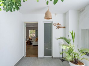 Um interior limpo e moderno, com uma luminária pendente de vime, uma planta em vaso e uma placa com a inscrição 'Villa Helena'.