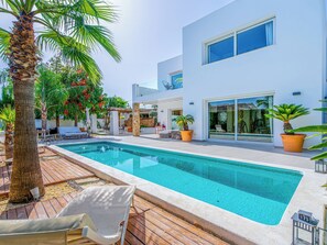 Uma área moderna à beira da piscina, com piscina transparente, espreguiçadeiras e plantas em vasos.