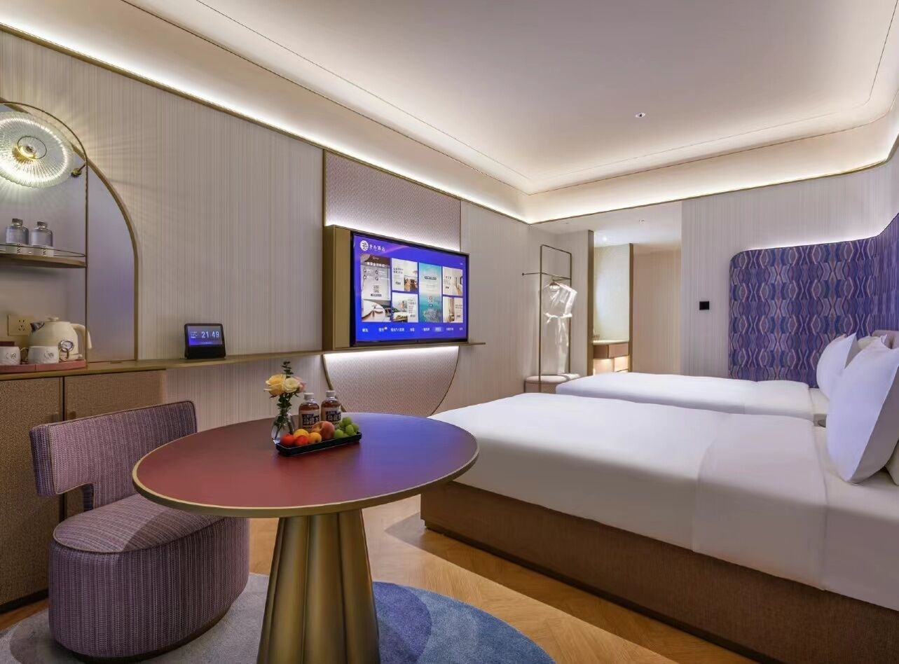 A modern hotel room with a bed, a TV, a dining table, and a seating area.