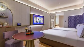 A modern hotel room with a bed, a TV, a dining table, and a seating area.