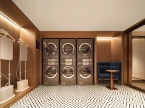 Quarto de hotel com design moderno, apresentando um espelho grande, uma área de estar azul e um conjunto de quatro máquinas de lavar embutidas.