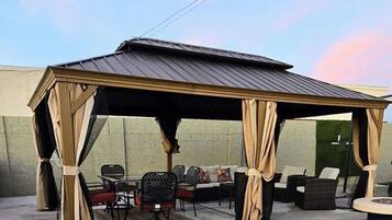A covered outdoor seating area with chairs and sofas, a table, and a pergola structure.