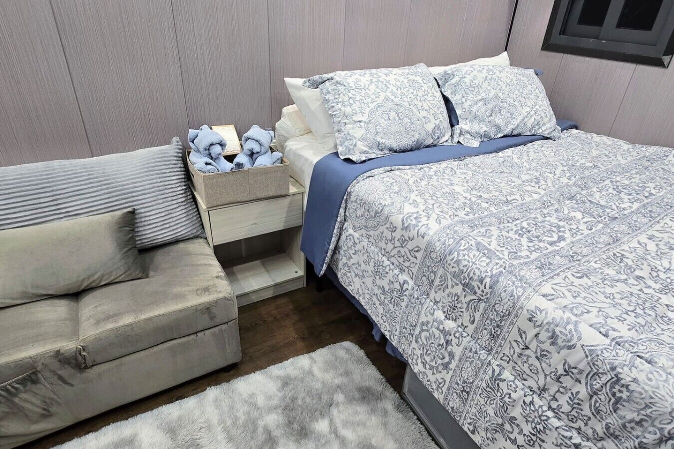 A bedroom with a bed, a nightstand, a sofa, and a rug.