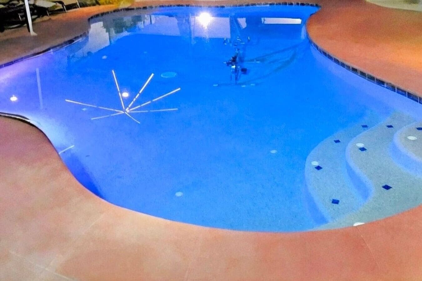 A swimming pool with a curved edge and a tiled deck surrounding it.