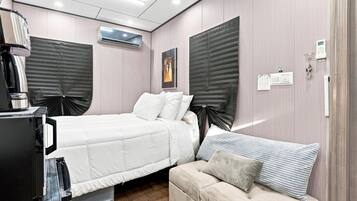 A bedroom with a bed, a sofa, a desk with a computer, and an air conditioning unit.