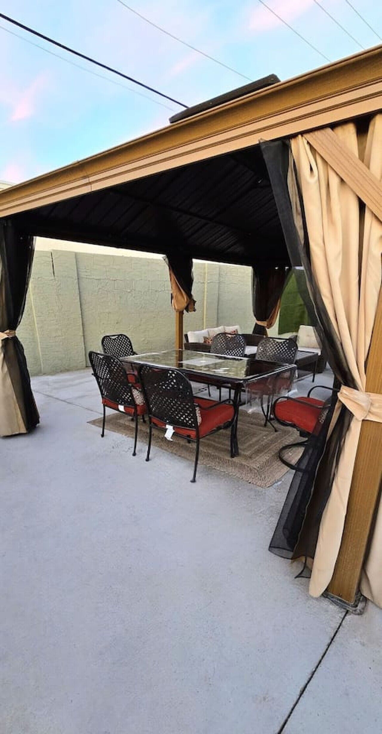 En udendørs terrasse med et bord og stole, et overdækket område og gardiner.