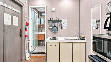 A modern kitchen with a built-in oven, a sink, and a stove. There is a fire extinguisher mounted on the wall and a sign indicating a shared kitchen area.