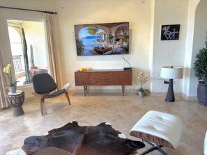 A living room with a large painting, a leather sofa, a dining table, and a potted plant. - Beachfront condo in Paradise 3 bed /2 bath (San José del Cabo)