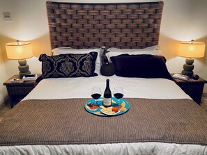 A neatly made bed with a brown headboard, two bedside lamps, and a tray with a bottle and glasses of red wine. - Beachfront condo in Paradise 3 bed /2 bath (San José del Cabo)