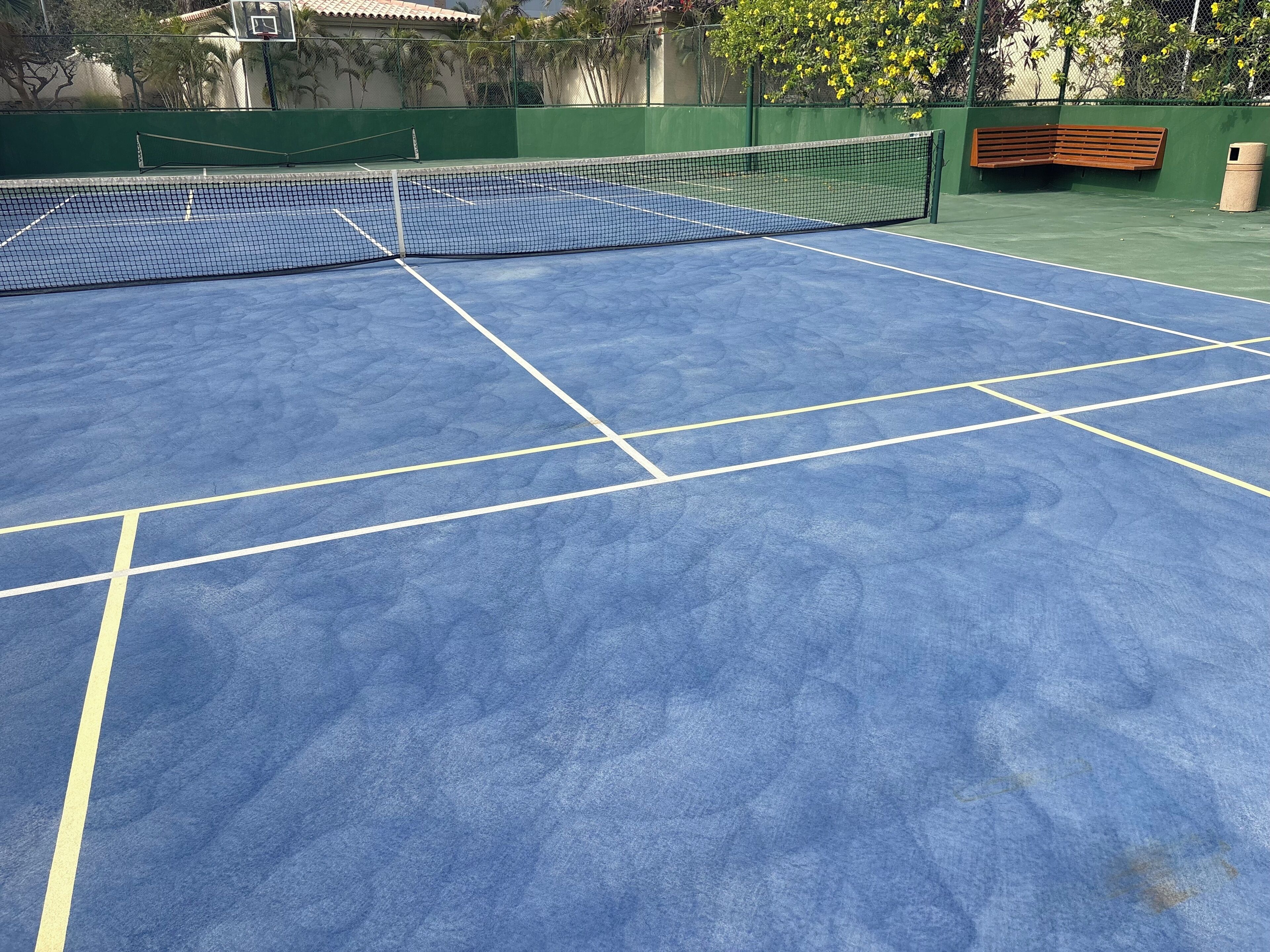 Un court de tennis avec un filet, des murs verts et un banc.