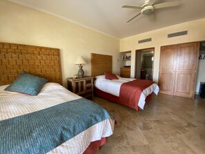 A hotel room with two beds, a ceiling fan, a bedside table with a lamp, a wooden headboard, a bathroom door, and a wardrobe. - Beachfront condo in Paradise 3 bed /2 bath (San José del Cabo)