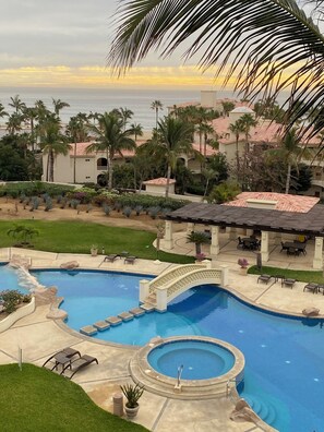 A swimming pool with a bridge, surrounded by palm trees and buildings with red-tiled roofs. - Beachfront condo in Paradise 3 bed /2 bath (San José del Cabo)