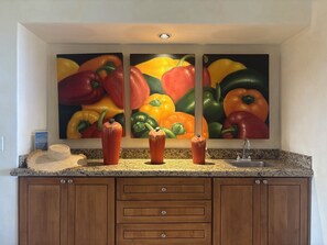 A kitchen with a granite countertop, wooden cabinets, and a wall-mounted painting of bell peppers. - Beachfront condo in Paradise 3 bed /2 bath (San José del Cabo)