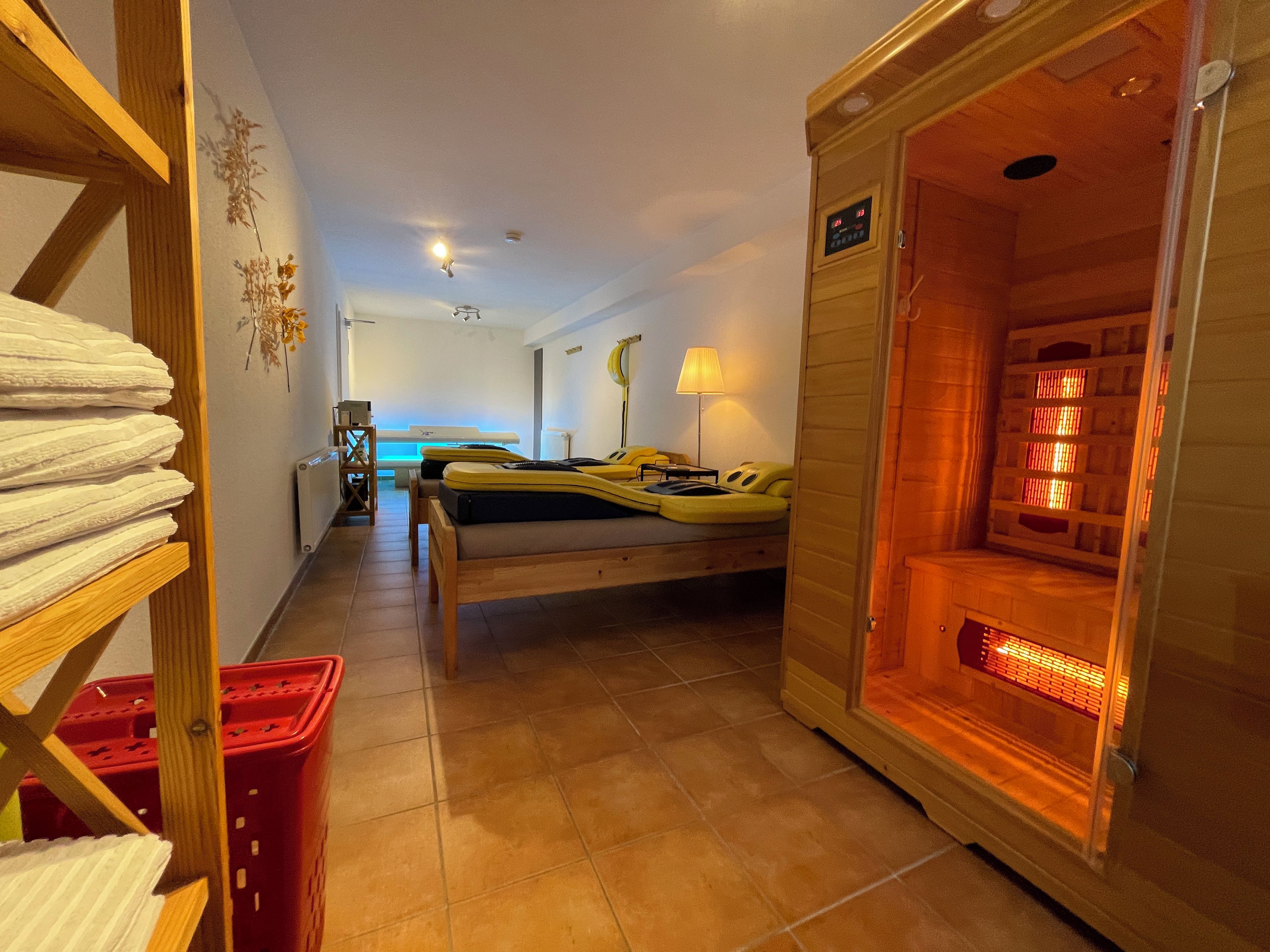 A room with a sauna, a bed, a bench, and a shelf with towels.