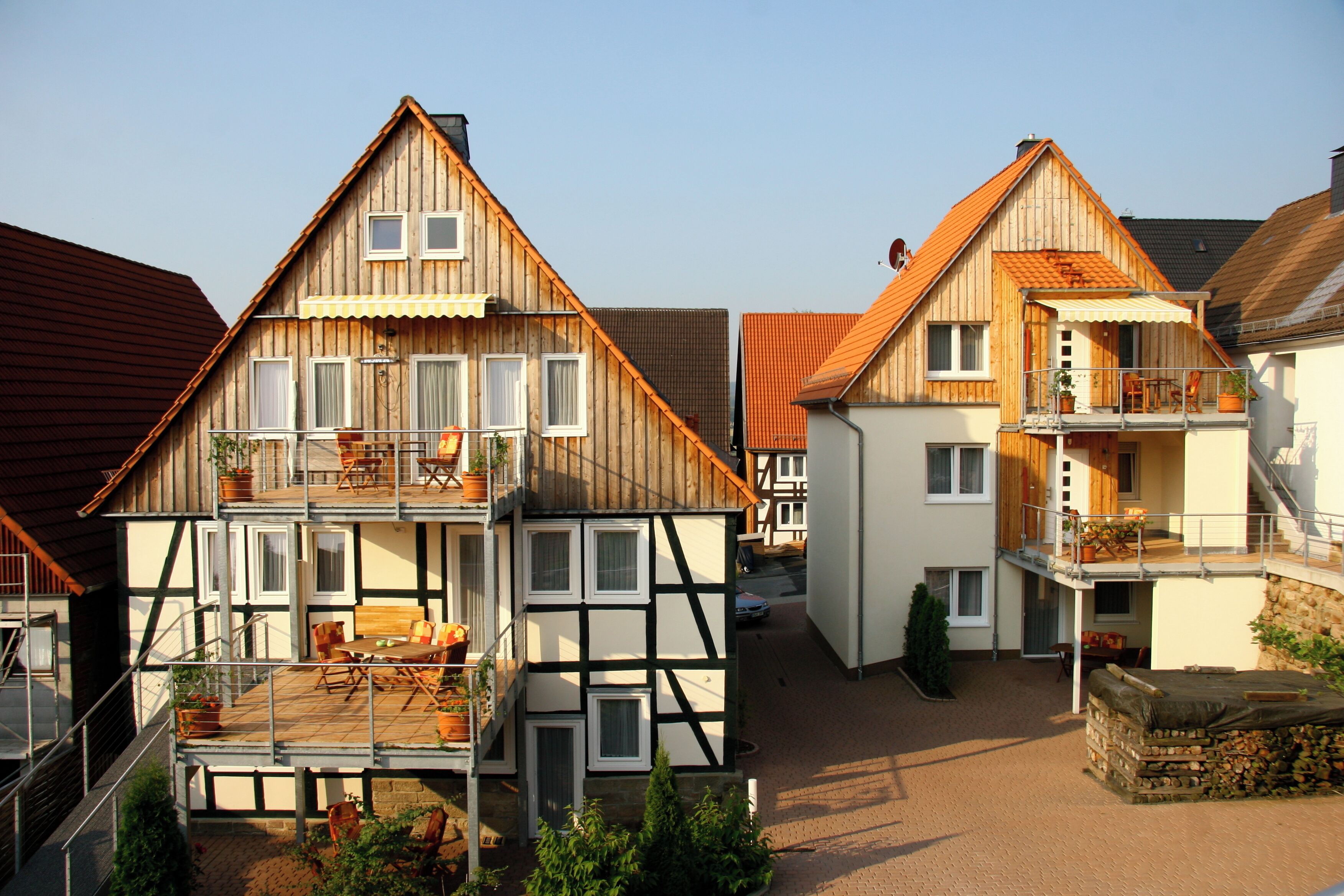 A traditional wooden house with a balcony, a lower level with a table and chairs, and a staircase leading to the upper floor.
