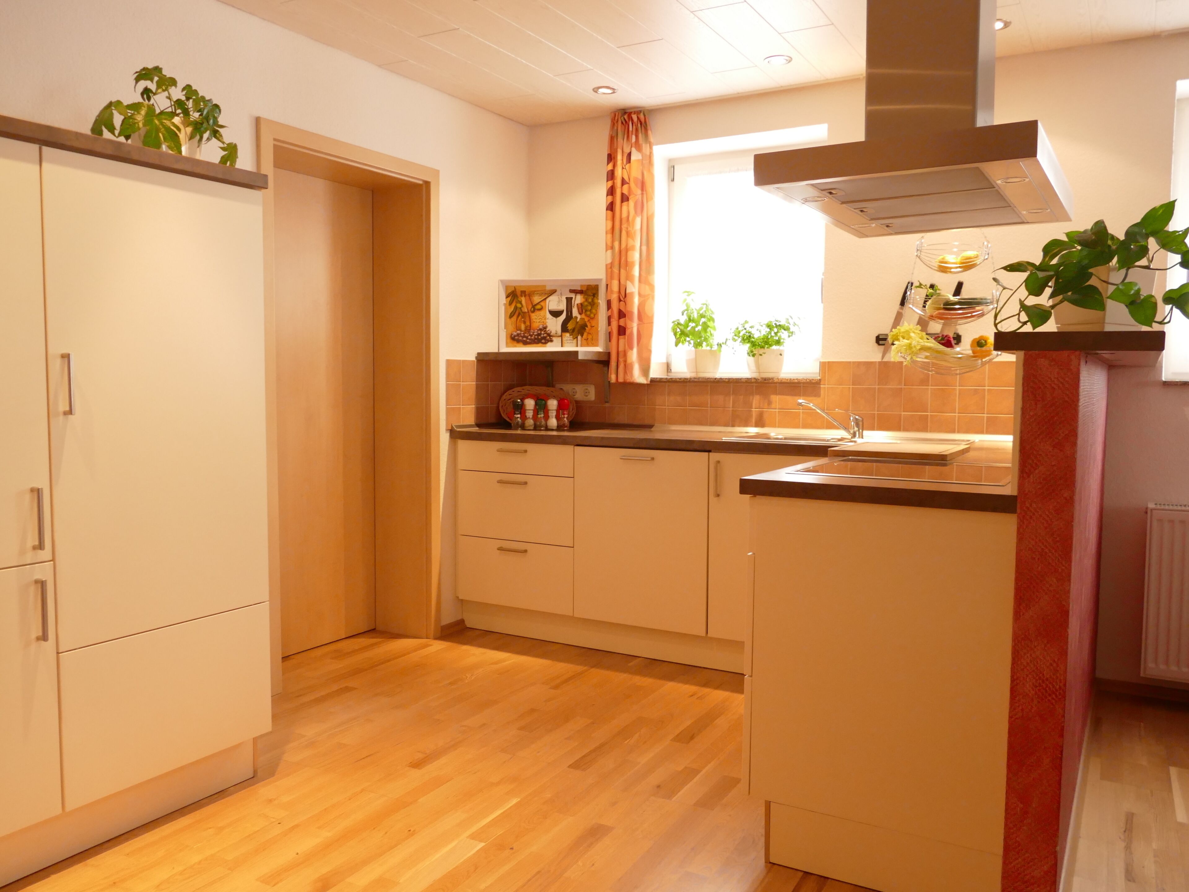Uma cozinha com piso de madeira, armários brancos, uma janela com cortinas e uma planta no balcão.