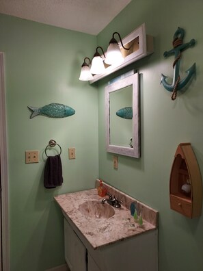 Une salle de bain avec un mur vert, un lavabo en marbre, un porte-serviettes, un miroir et une ancre décorative.