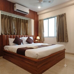 Quarto de hotel com cama de madeira, mesa de cabeceira com abajur e janela com cortinas.