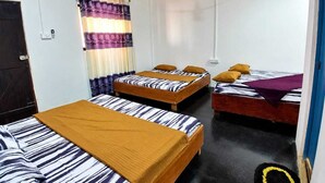 Quarto com três camas de madeira, um ventilador de teto e janela com cortinas.
