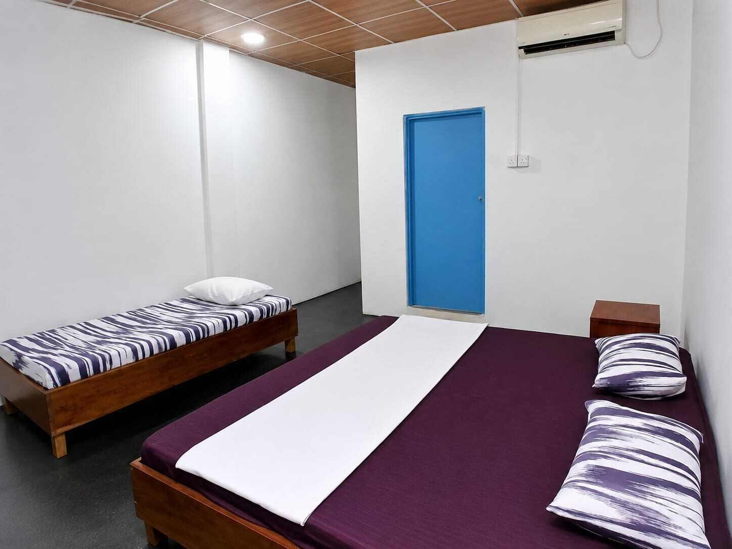 Una habitación con dos camas individuales, una cama grande, una puerta azul y un equipo de aire acondicionado.