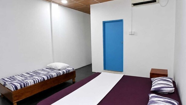 Quarto com duas camas de solteiro, uma cama grande, uma porta azul e um aparelho de ar condicionado.