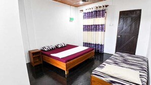 Quarto com duas camas, piso de madeira, ventilador de teto e uma porta.