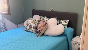 A bed with a teal bedspread and multiple pillows, a wooden nightstand with a lamp, and a starfish decoration on the wall. - House with a garden in Santa Teresa di Gallura (Santa Teresa di Gallura)
