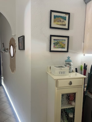 A hallway with a white wall, a framed picture, a mirror, and a small white cabinet with drawers. - House with a garden in Santa Teresa di Gallura (Santa Teresa di Gallura)